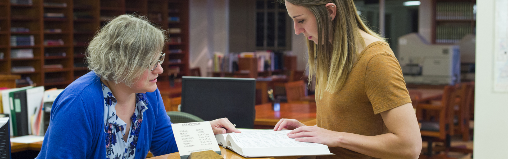 Woman at help desk looking at book with a student.